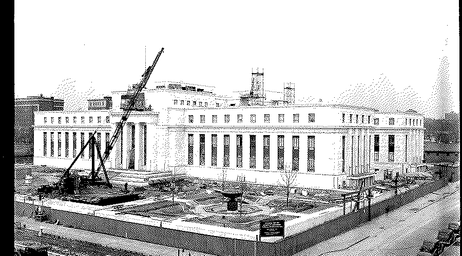 The new Federal Reserve Board building in Washington in 1937: a long white building with tall columns, a construction crane at its side and a fenced lot in front.