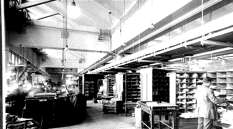 A mail sorting room at the US Post Office in Washington with long banks of pigeonholes and a worker at a sorting table.