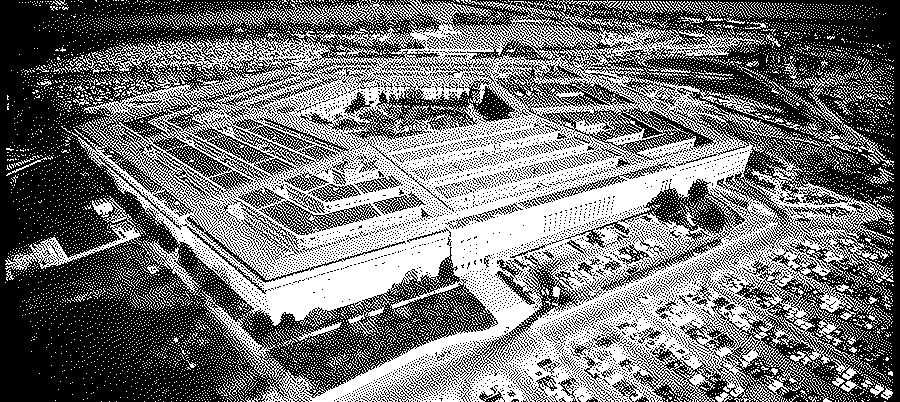 Aerial view of the Pentagon with its rings and courtyard, large car parks beside it and a road in the foreground.