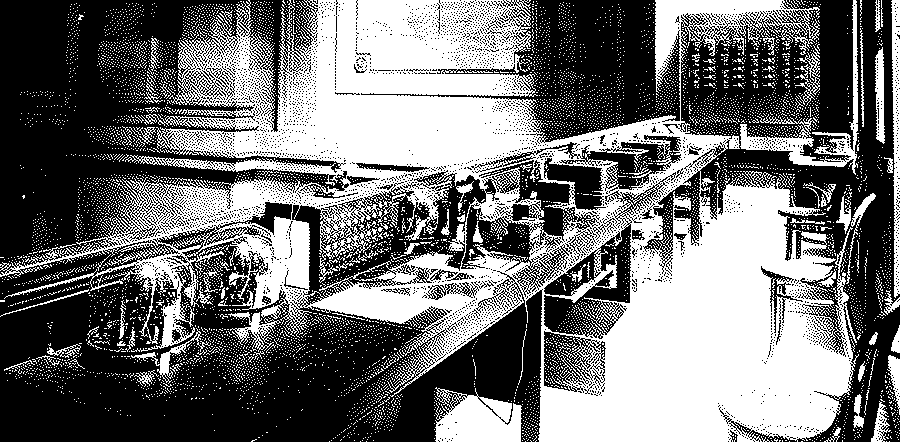 A long wooden table on a mezzanine at the New York Stock Exchange with ticker-tape machines under glass domes, telephones, a switchboard and bentwood chairs by the tall windows.